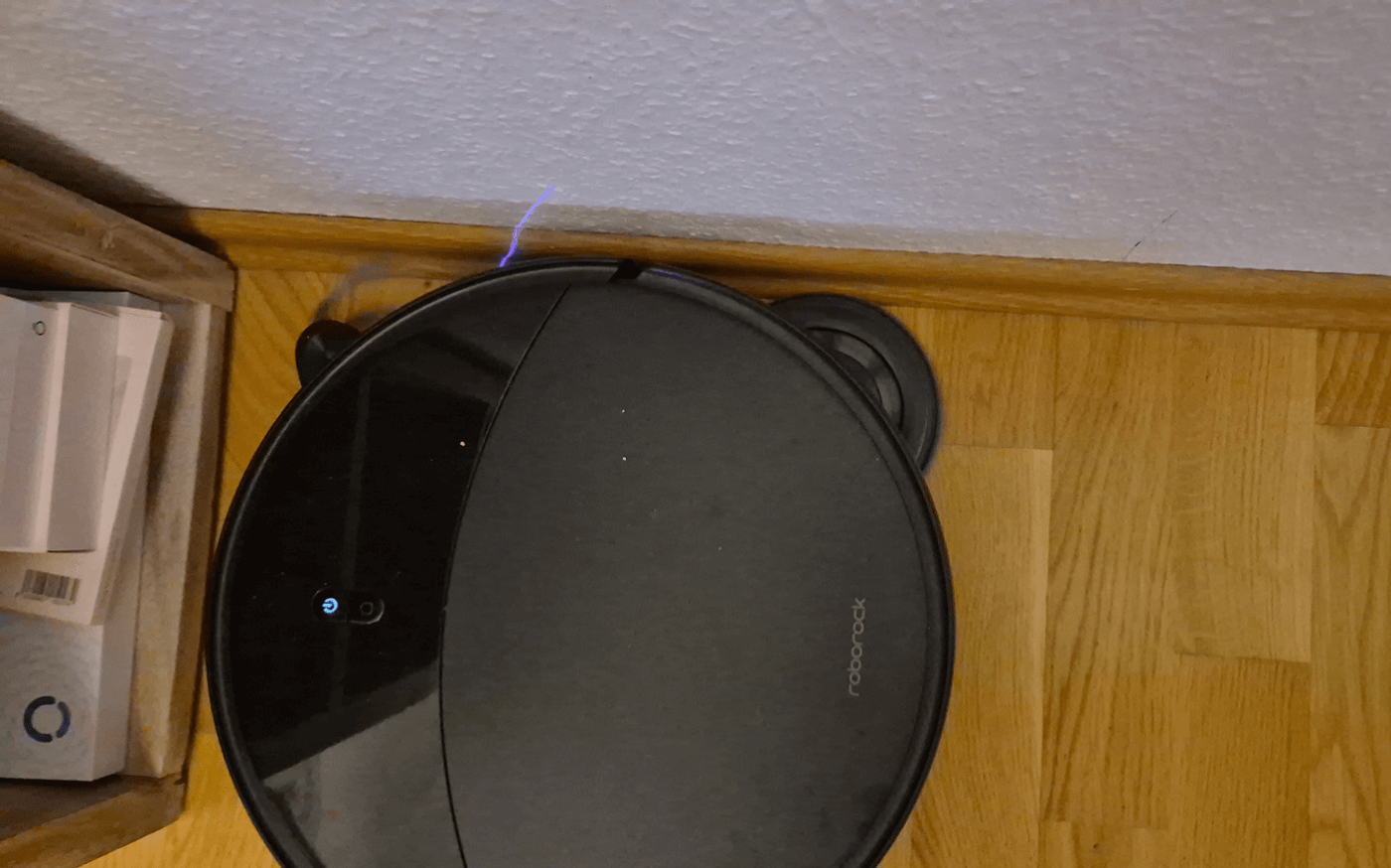 Der Roborock Saros 20 wischt dicht entlang einer weißen Leiste im Wohnzimmer.